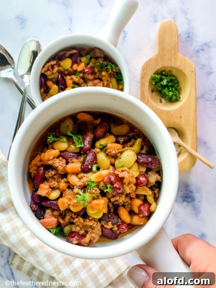 A close-up of a bowl of delicious Instant Pot calico beans, with another bowl and a wooden bowl of spices in the background.