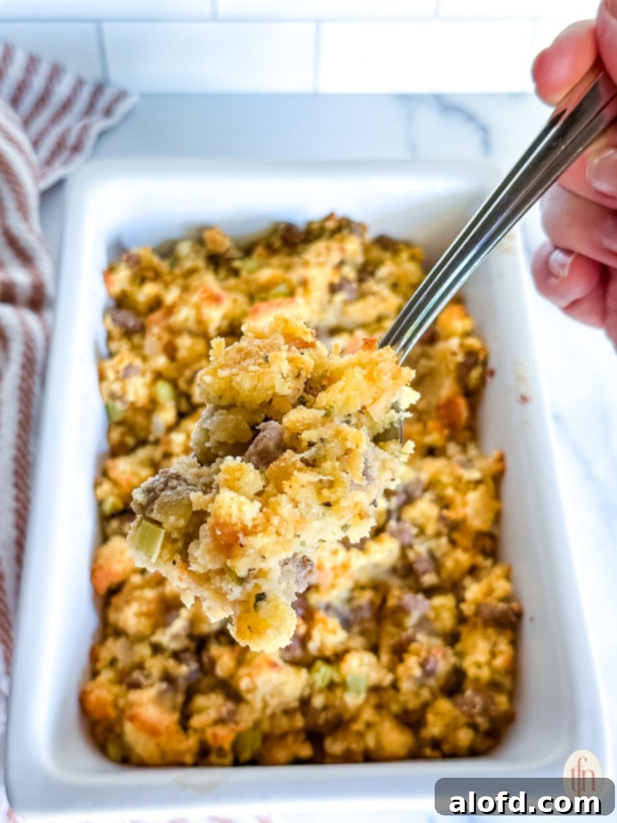 A spoonful of Jiffy Cornbread Dressing being lifted from a white serving dish, showing its delicious texture.