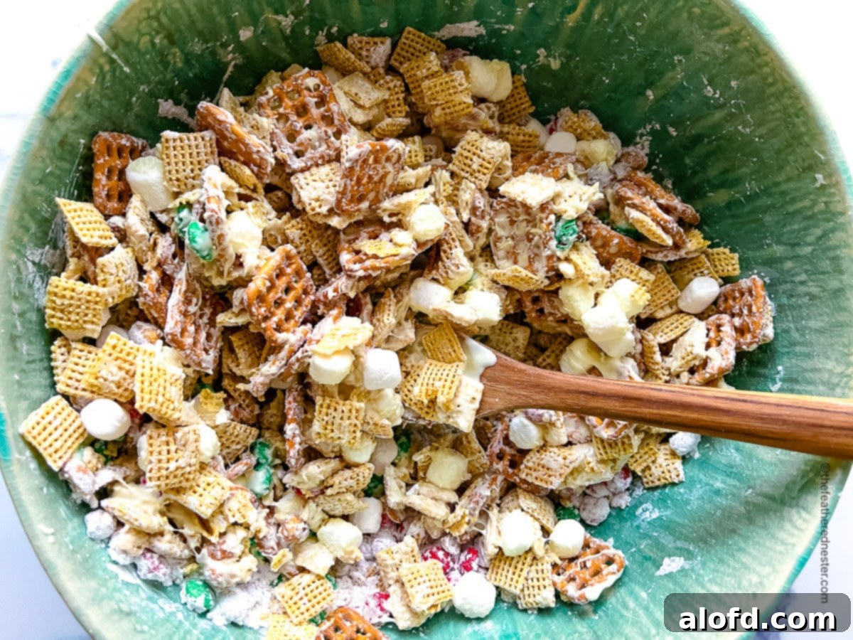 horizontal photo of a green bowl with Chex Mix being stirred by a wooden spoon.