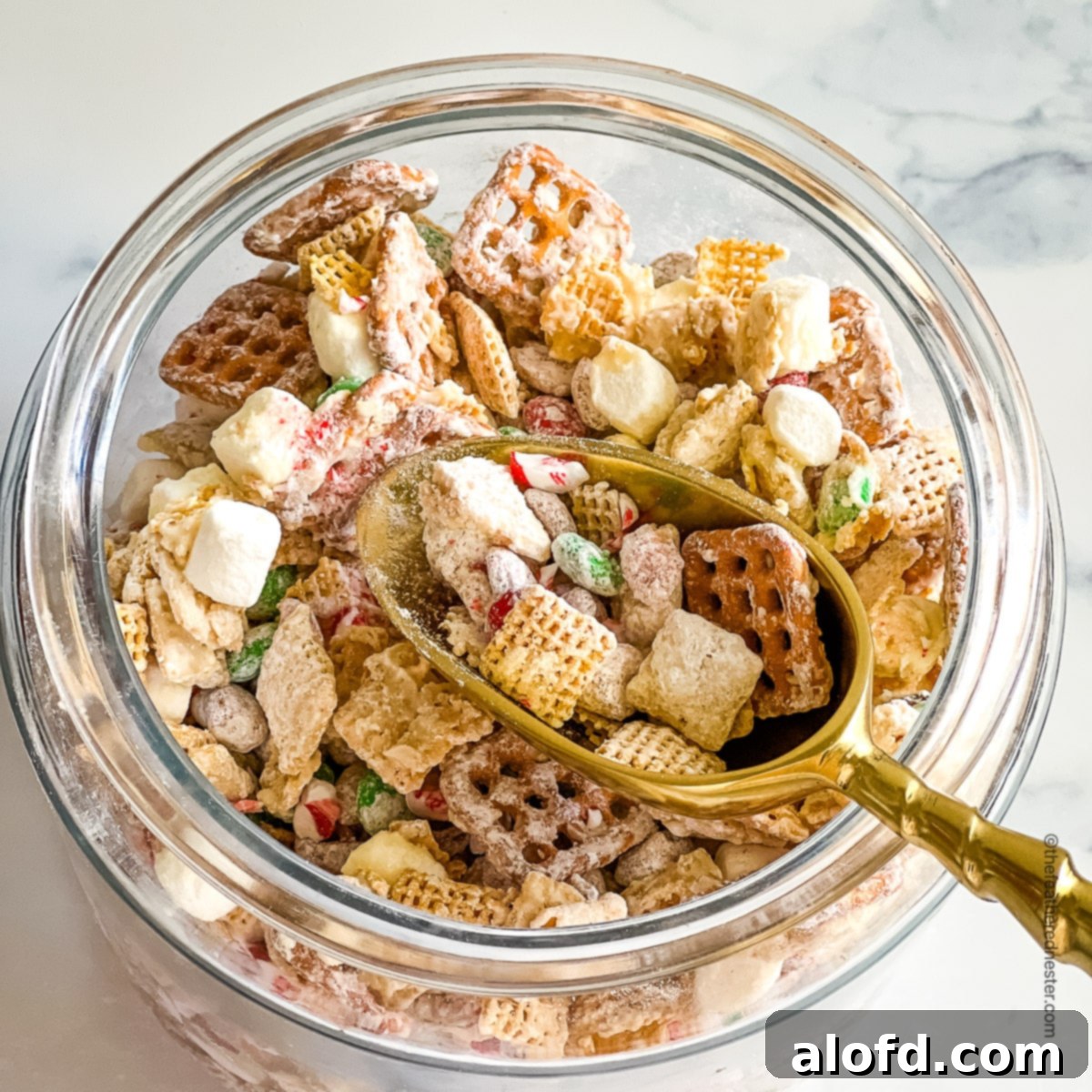 a jar with Christmas Chex Mix with a golden scoop.