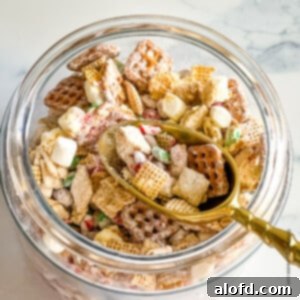 A jar with Christmas Chex Mix with a golden scoop.