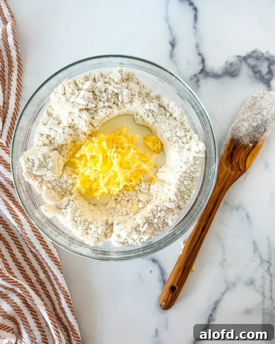 A mixing bowl containing baking mix, grated cold butter, and buttermilk, ready to be combined into biscuit dough.