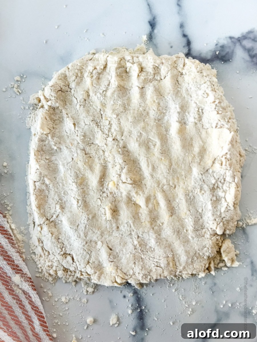 A close-up view of biscuit dough being folded into thirds on a floured surface, demonstrating a key step for creating flaky layers.