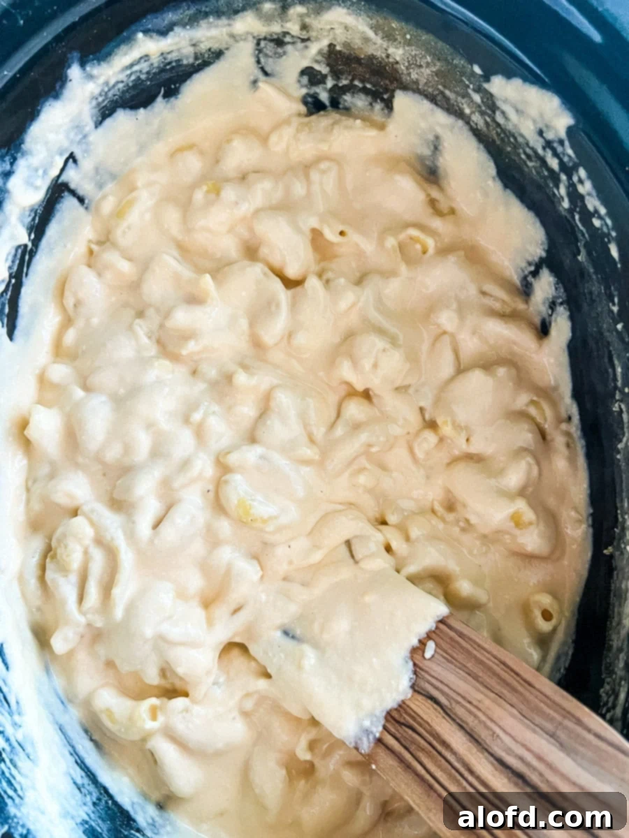 using a wooden spoon to stir 3 cheese mac and cheese in a crock pot.