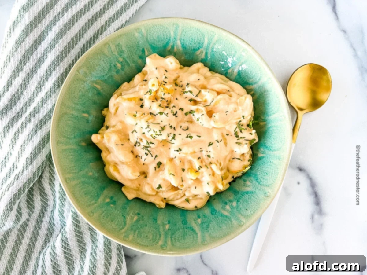 horizontal photo of slow cooker mac and cheese with cream cheese in a green bowl with a spoon at the side.