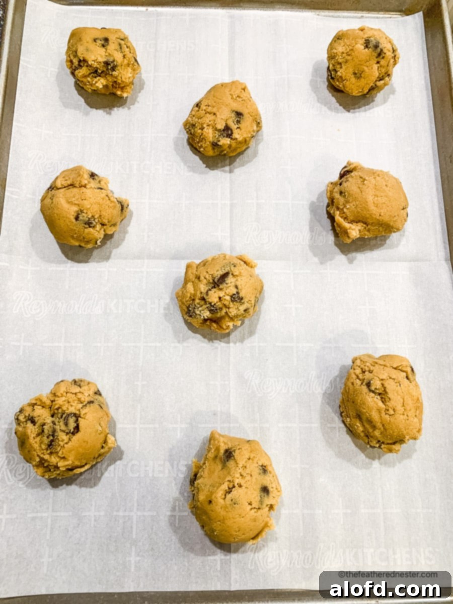 Evenly sized cookie dough balls are neatly arranged on a parchment paper-lined baking sheet, spaced apart for optimal baking.