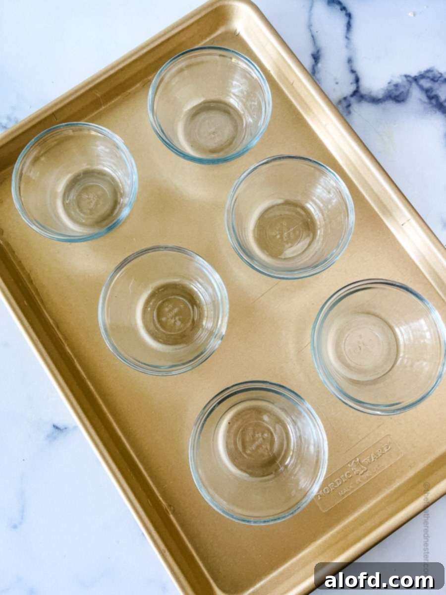 Small clear glass ramekins placed neatly on a baking sheet, ready for the custard mixture.