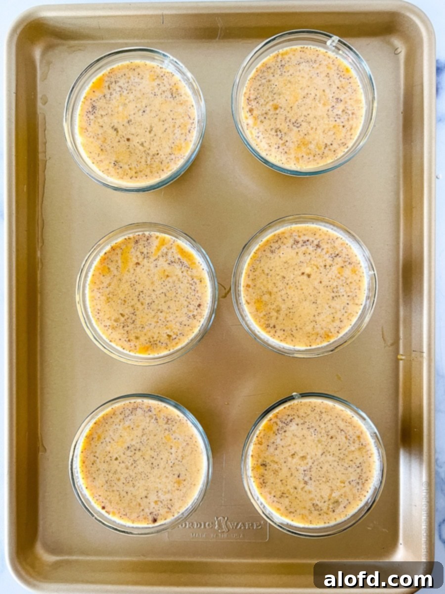 Unbaked pumpkin custard mixture in small glass bowls, carefully arranged on a baking sheet.