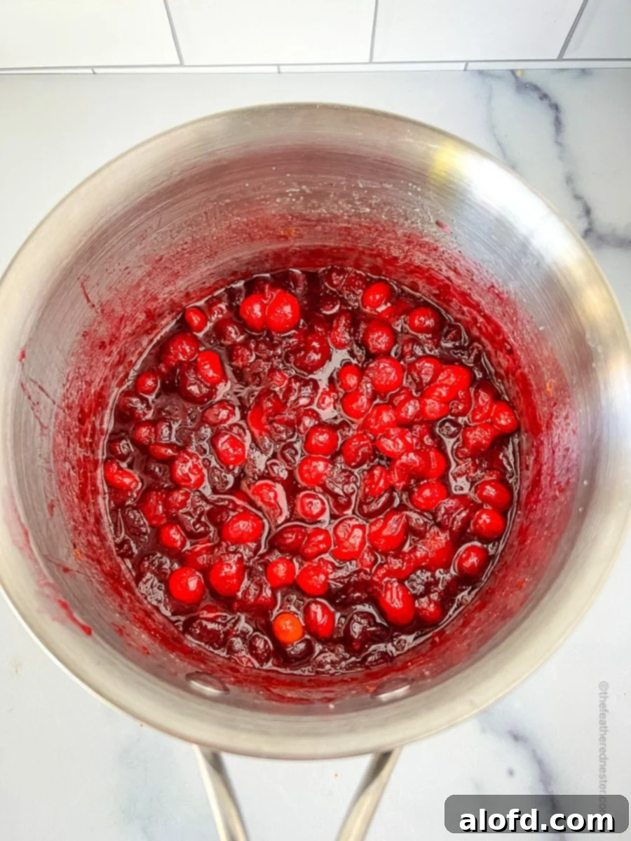 Bright red cranberries bursting and simmering in a large pot, thickening into a rich sauce.