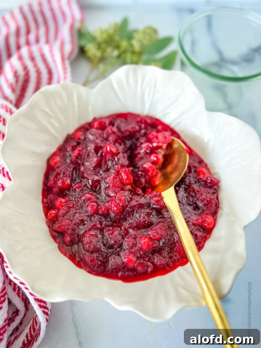 A beautifully cooled and thickened bowl of fresh cranberry sauce with orange juice, ready to be served, accompanied by a gold serving spoon.
