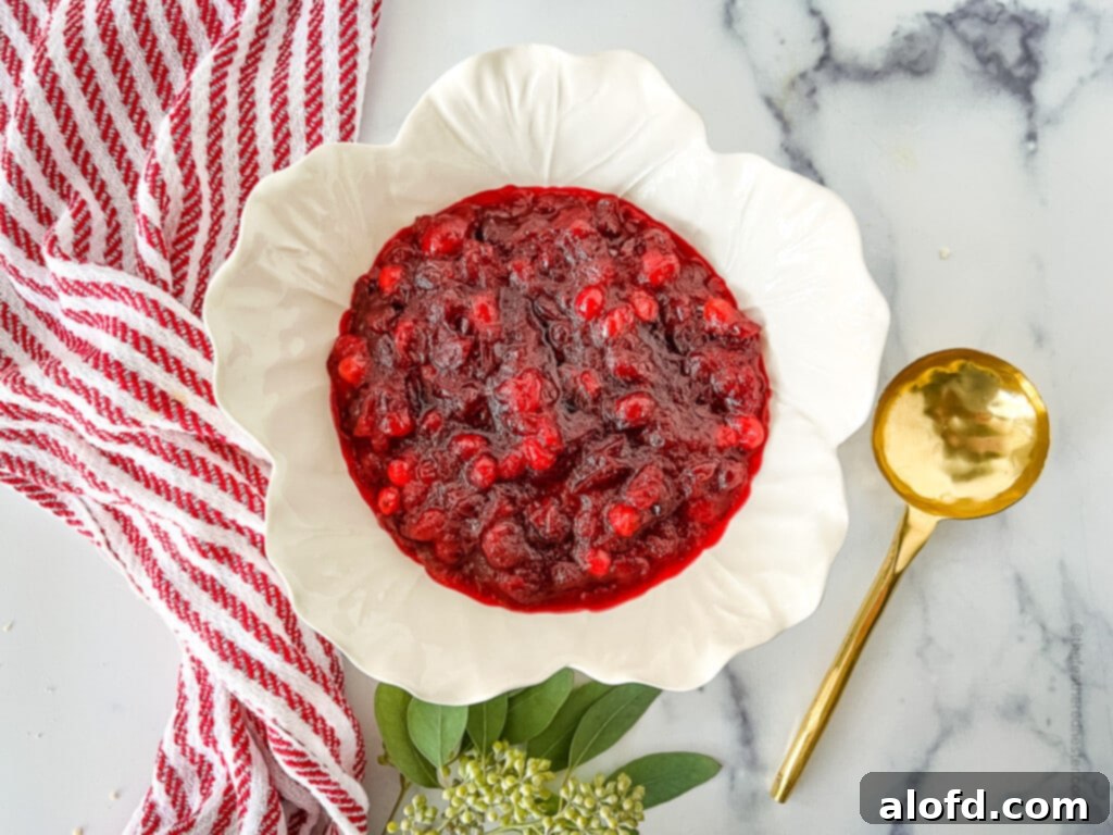 A white bowl filled with glistening, thick homemade cranberry sauce with visible orange zest, ready to be enjoyed.