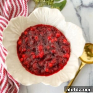 A white bowl of perfectly cooled and thickened fresh cranberry sauce ready to serve, with a gold serving spoon nestled within.
