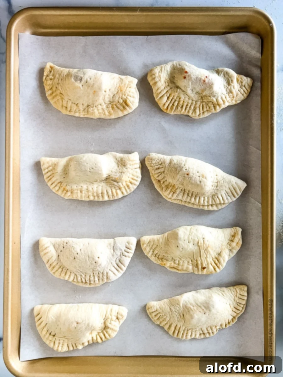 Savory Pepperoni Calzone Pockets 13 Eight unbaked mini pepperoni calzones neatly arranged on a baking sheet, brushed with egg wash and ready for the oven.