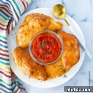 Savory Pepperoni Calzone Pockets 16 Top view photo of a white plate with Mini Pepperoni Calzones and marinara dipping sauce at the center.