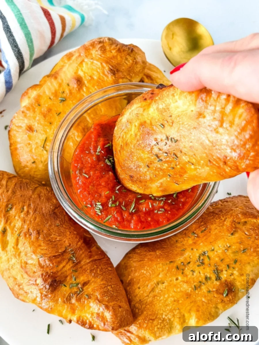 Savory Pepperoni Calzone Pockets 3 A hand dipping a homemade calzone into a bowl of rich marinara sauce.
