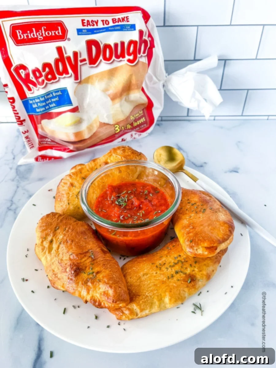 Savory Pepperoni Calzone Pockets 4 A white plate featuring Mini Pepperoni Calzones with a bowl of marinara dipping sauce in the center, and a bag of Bridgford's Ready-Dough in the background.