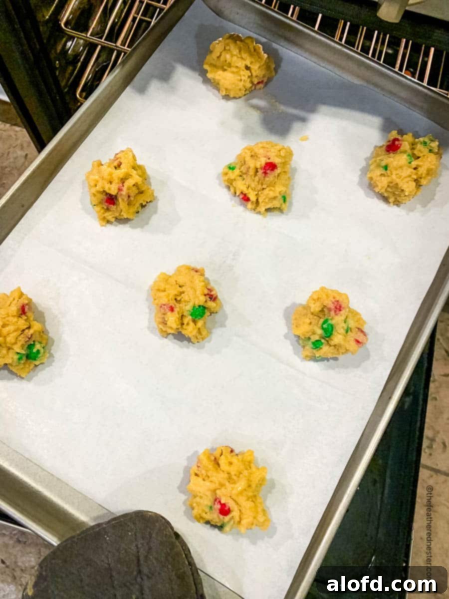 Festive M and M Christmas Cookies 6 A parchment paper lined baking sheet with unbaked cookie dough balls.