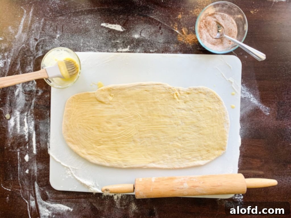 Spreading softened butter onto the rolled-out pumpkin spice bread dough with a pastry brush.