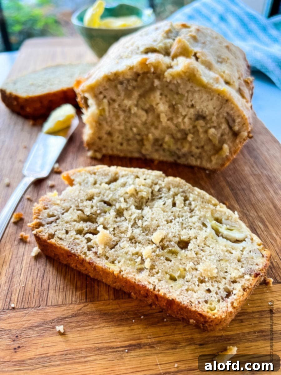 A perfectly sliced piece of moist Bisquick banana bread in front of the warm, golden loaf.
