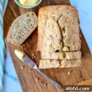 Square photo of a warm loaf of Bisquick Banana Bread with butter and a bread knife.