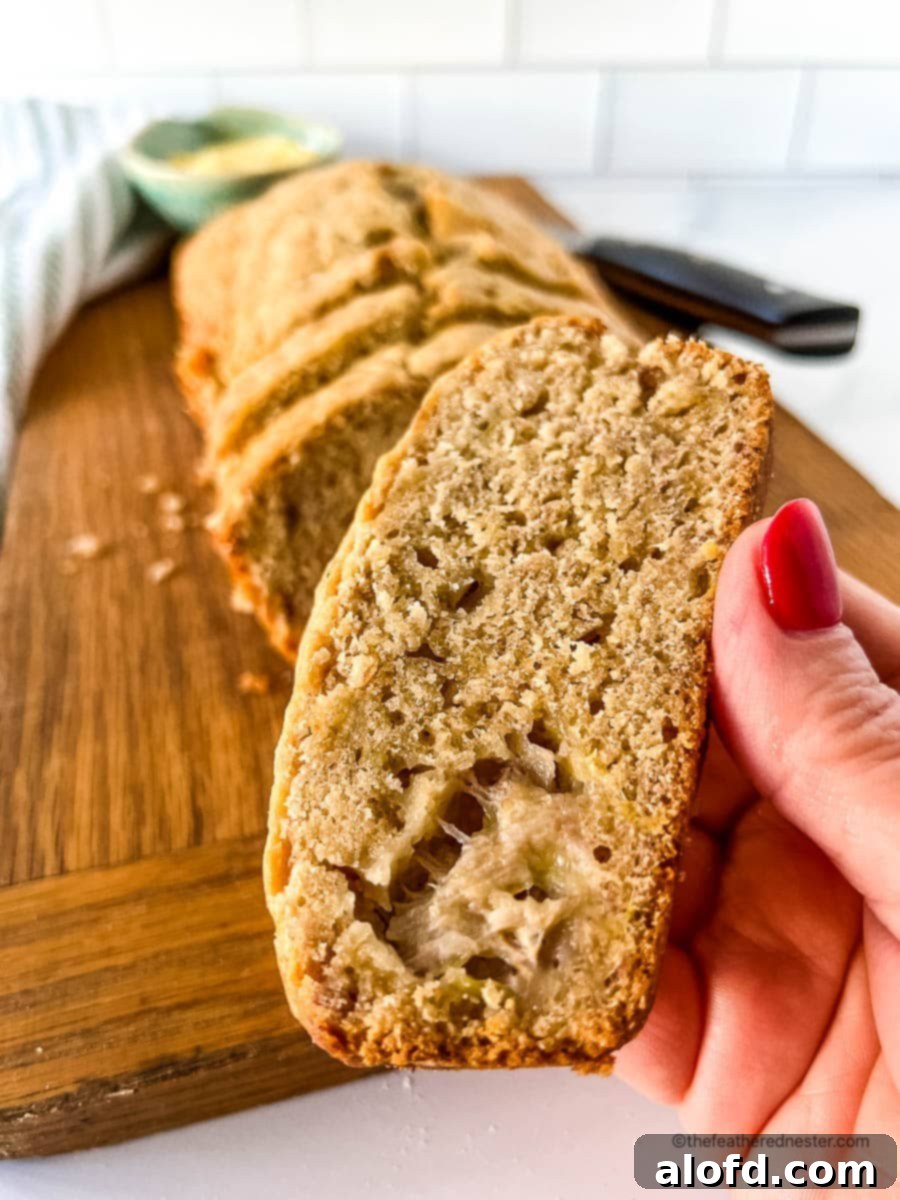 A hand reaching for a slice of golden Bisquick banana bread from a freshly baked loaf.
