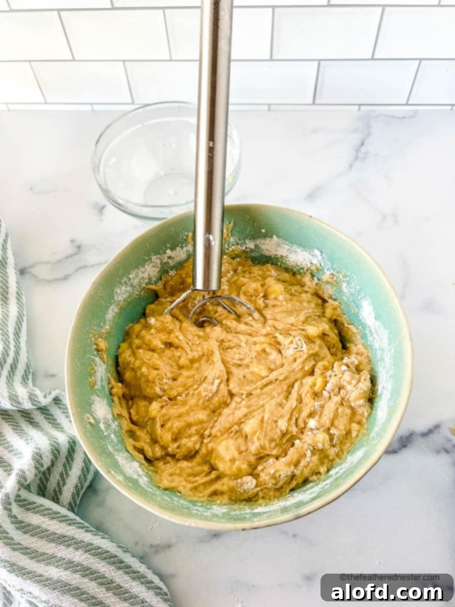 All Bisquick banana bread ingredients thoroughly combined in a green mixing bowl with a whisk.