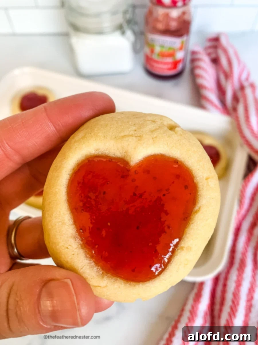 A hand holding buttery cookie filled with strawberry preserves.