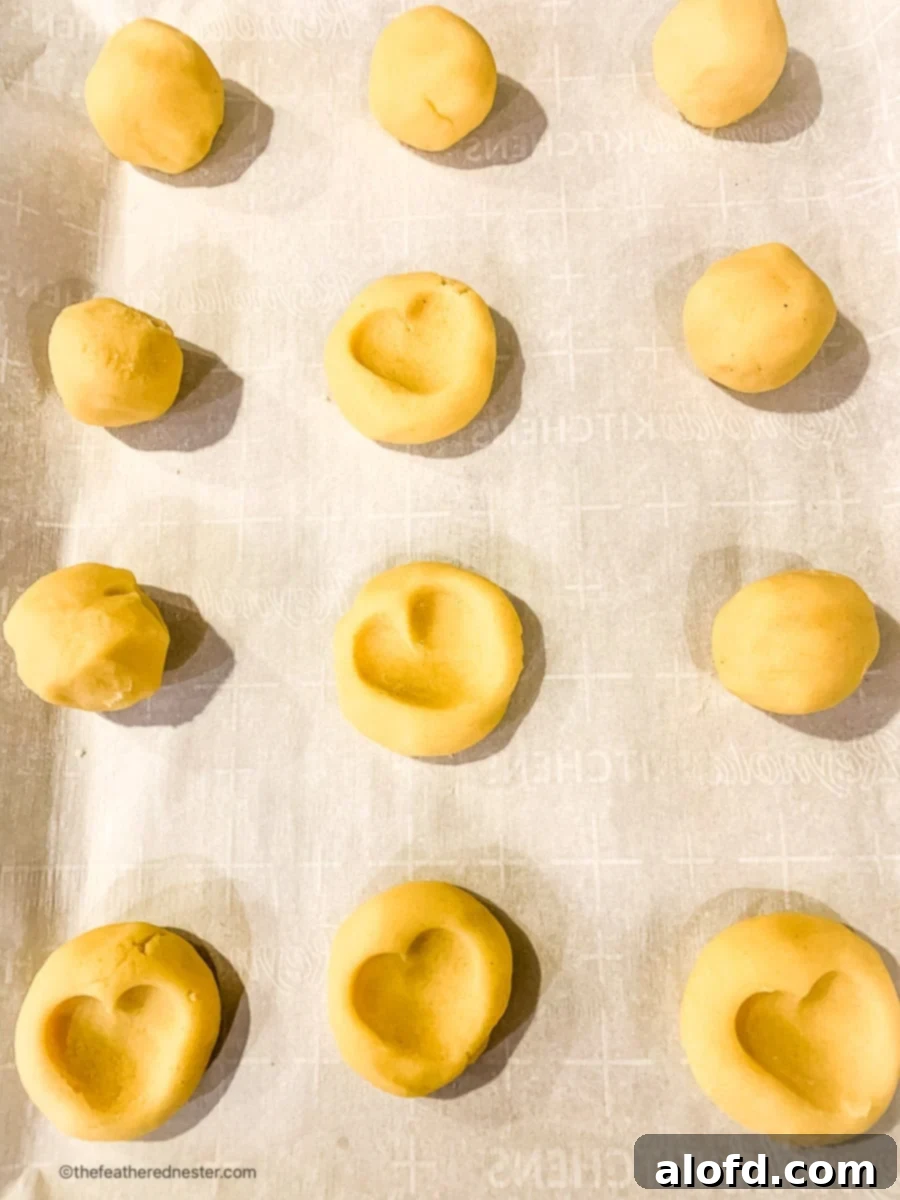 Unbaked thumbprint heart cookies on parchment lined baking sheet