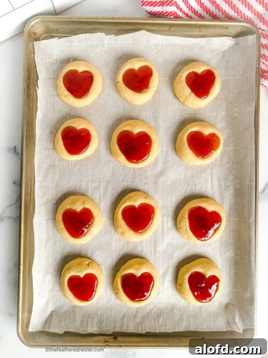 Cookies with jam thumbprints placed on a parchment paper lined baking sheet.