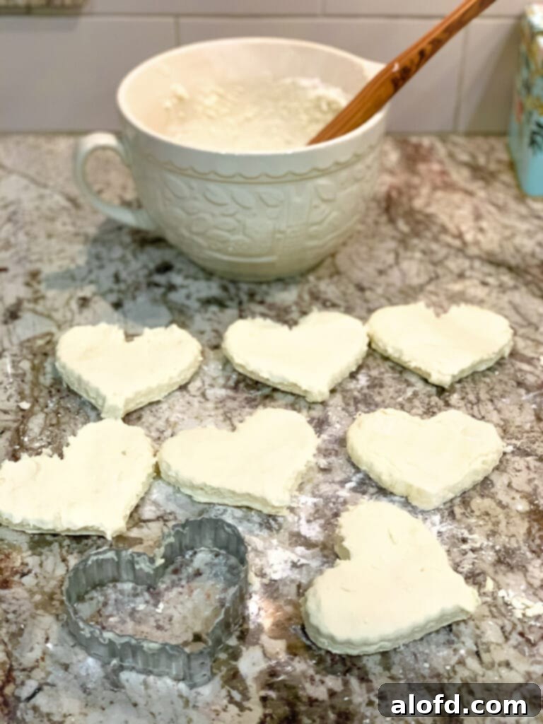 Rows of unbaked, perfectly heart-shaped biscuits, neatly arranged on a lightly floured countertop, awaiting their transformation into a golden, flaky Valentine's Day breakfast treat.