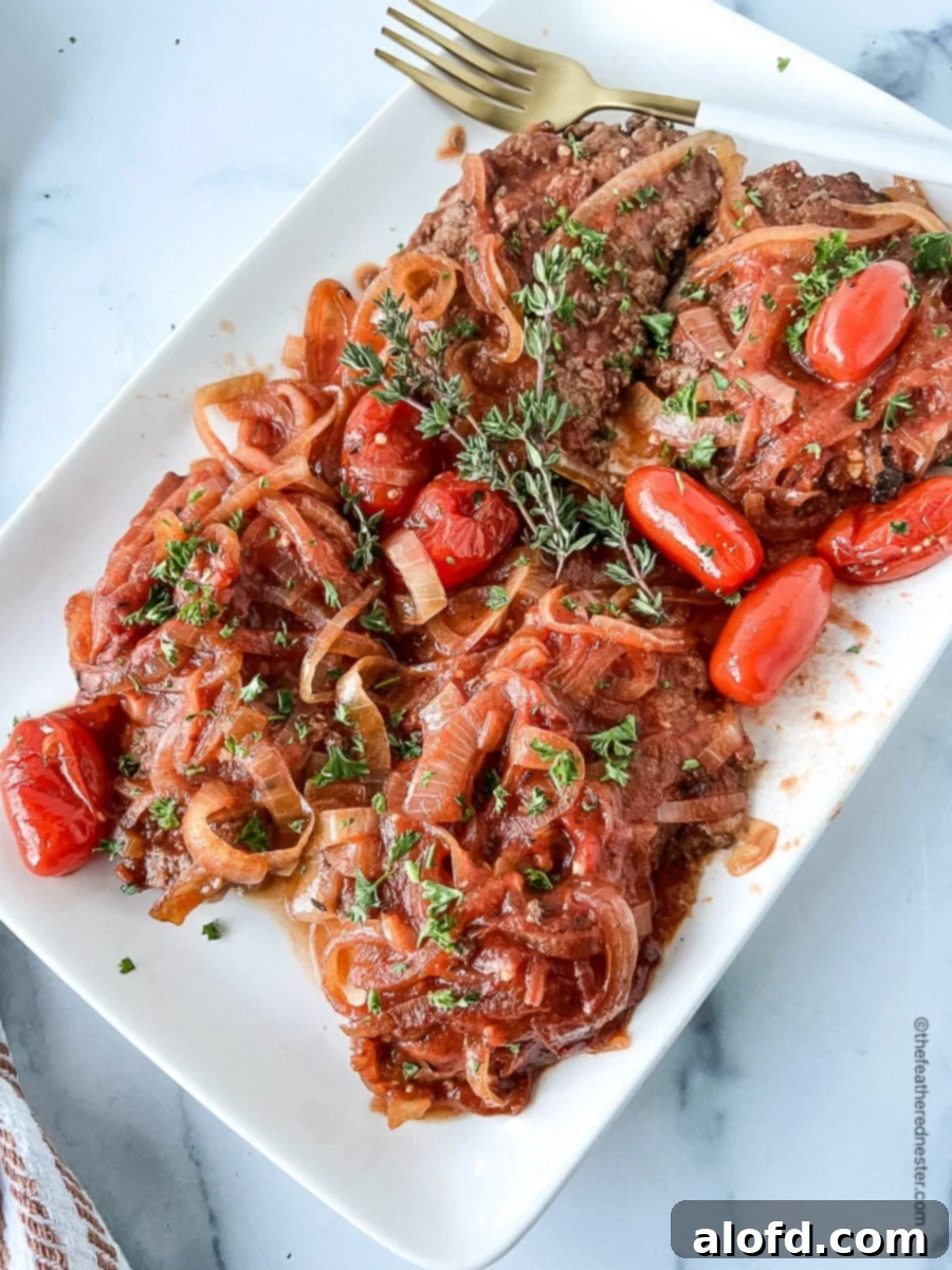 Tender Slow Cooker Swiss Steak 2 Crockpot Swiss steak with onions and tomatoes on a platter.