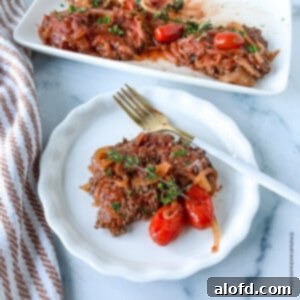 Tender Slow Cooker Swiss Steak 9 single serving of Swiss steak with onions and tomatoes on a white plate and more on a serving platter behind it.