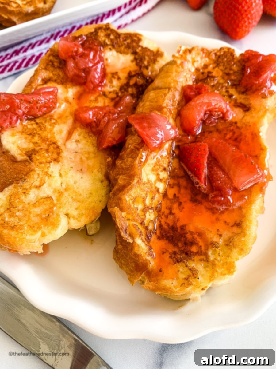 Luscious Strawberry French Toast 11 Close-up of two slices of strawberry French toast on a plate, garnished with fresh berries.