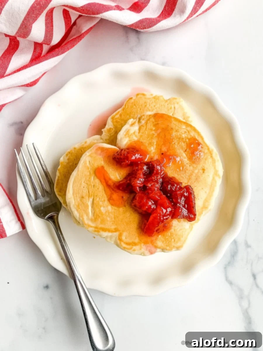 Table set with romantic breakfast of pancakes for 2. Heart shaped pancakes are a delicious and easy way to show your loved one how much you care. This recipe makes a short stack of pancakes, perfect for two people. These fluffy little pancakes are perfect for a cozy morning spent with your sweetheart and celebrating love on Valentine's morning!