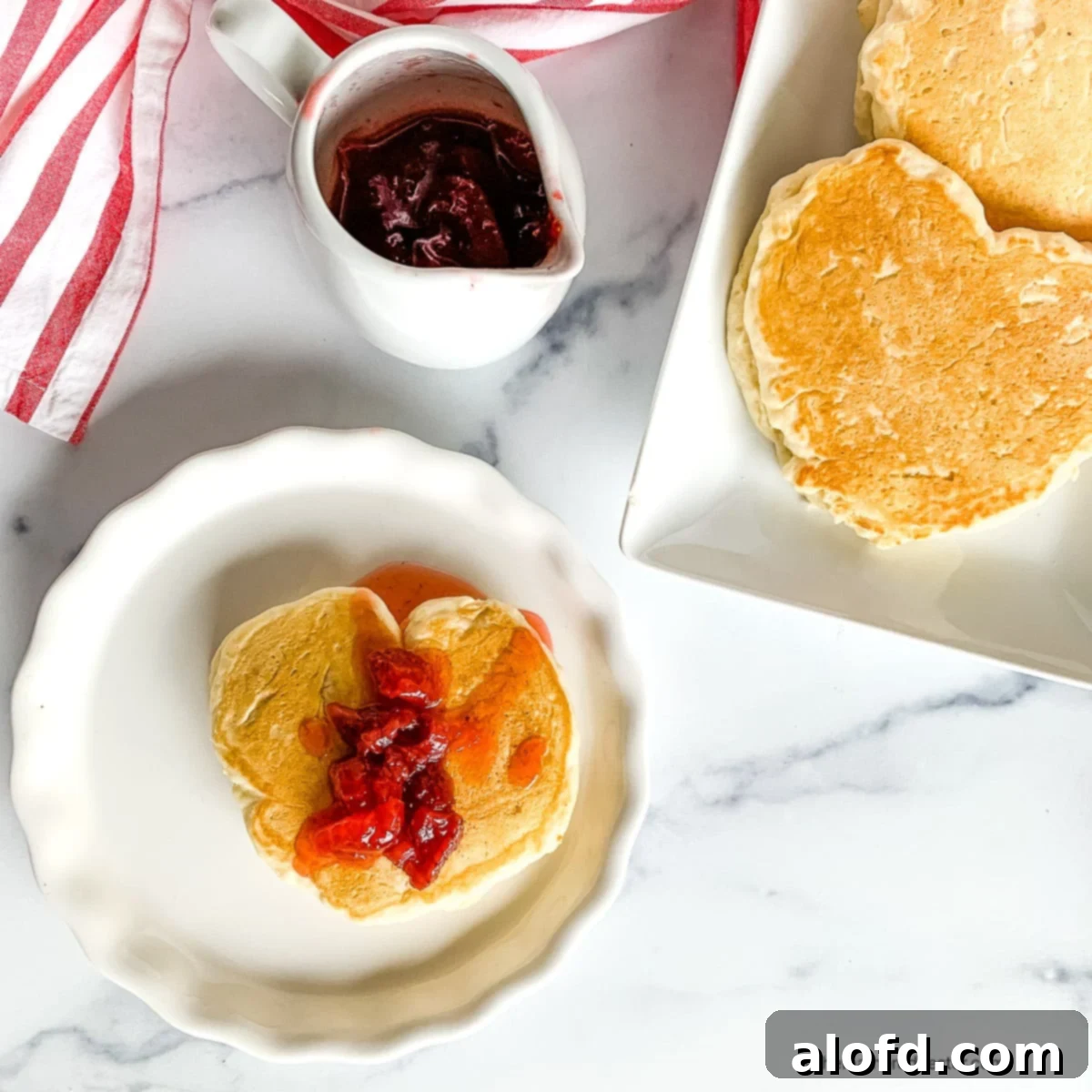Plated romantic breakfast of heart shaped pancakes for two. Start your Valentine's Day with love by making heart-shaped pancakes for two! This delicious and cozy breakfast is perfect for your sweetheart, especially when served with strawberry pancake syrup. A sweet way to kick off your special day together!