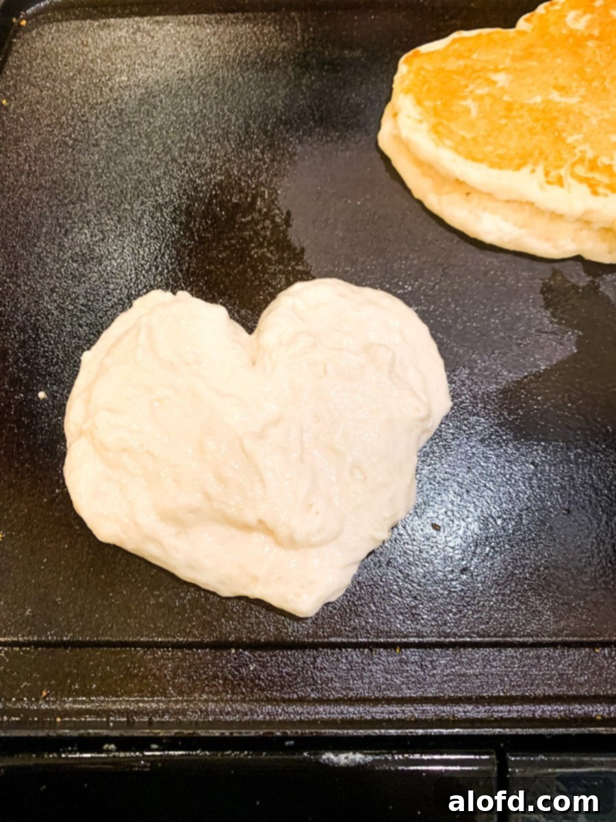 A heart shaped pancake cooking on a griddle.