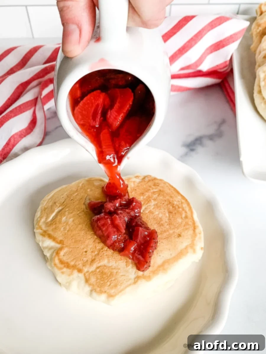 Pouring fresh strawberry syrup over a short stack of flapjacks.