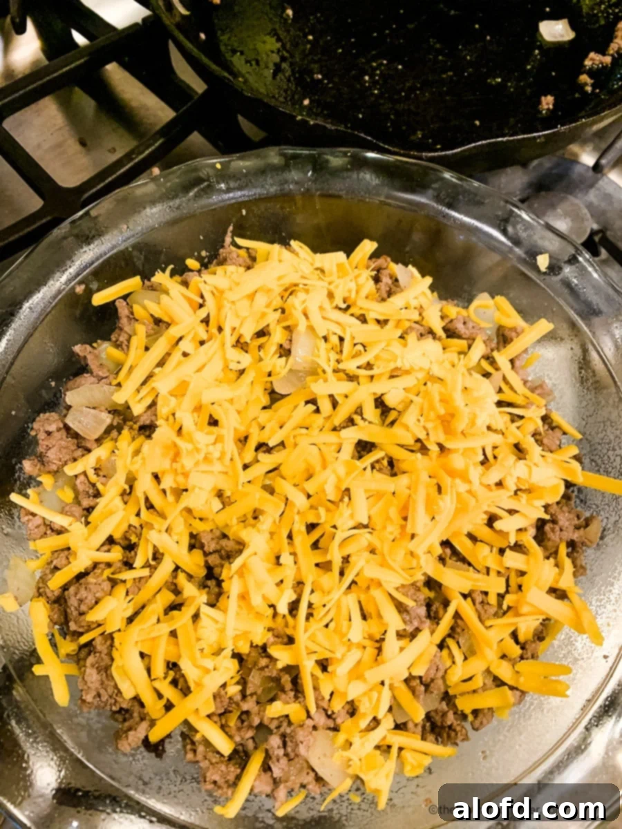 Hearty Bisquick Cheeseburger Bake 6 Shredded cheddar cheese on top of ground beef in a glass baking dish.