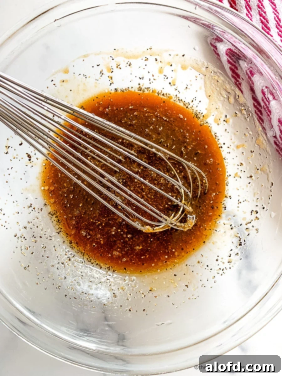 Whisking pork marinade ingredients in a glass mixing bowl, highlighting the fresh ginger and soy sauce.