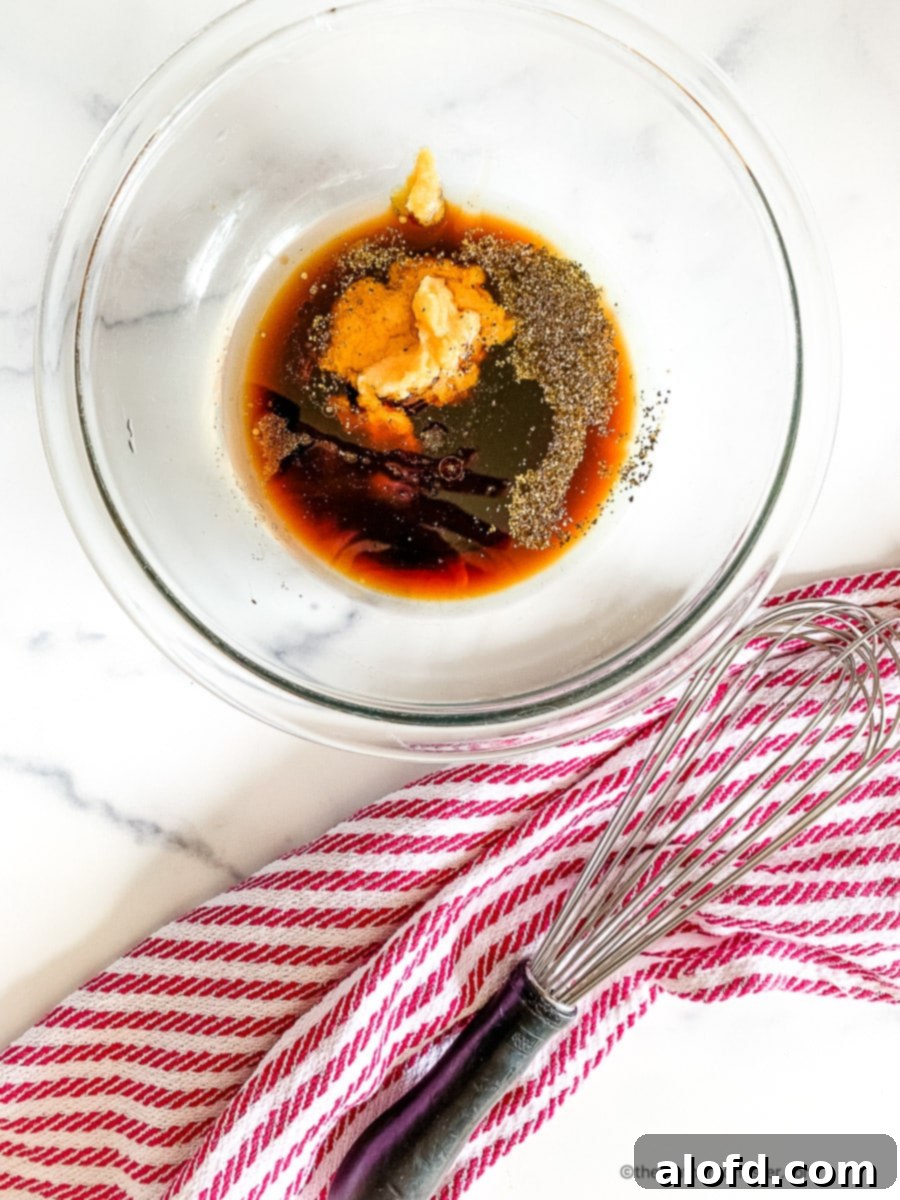 Fresh ginger and soy sauce in a glass mixing bowl with spices, ready to be whisked for marinade.