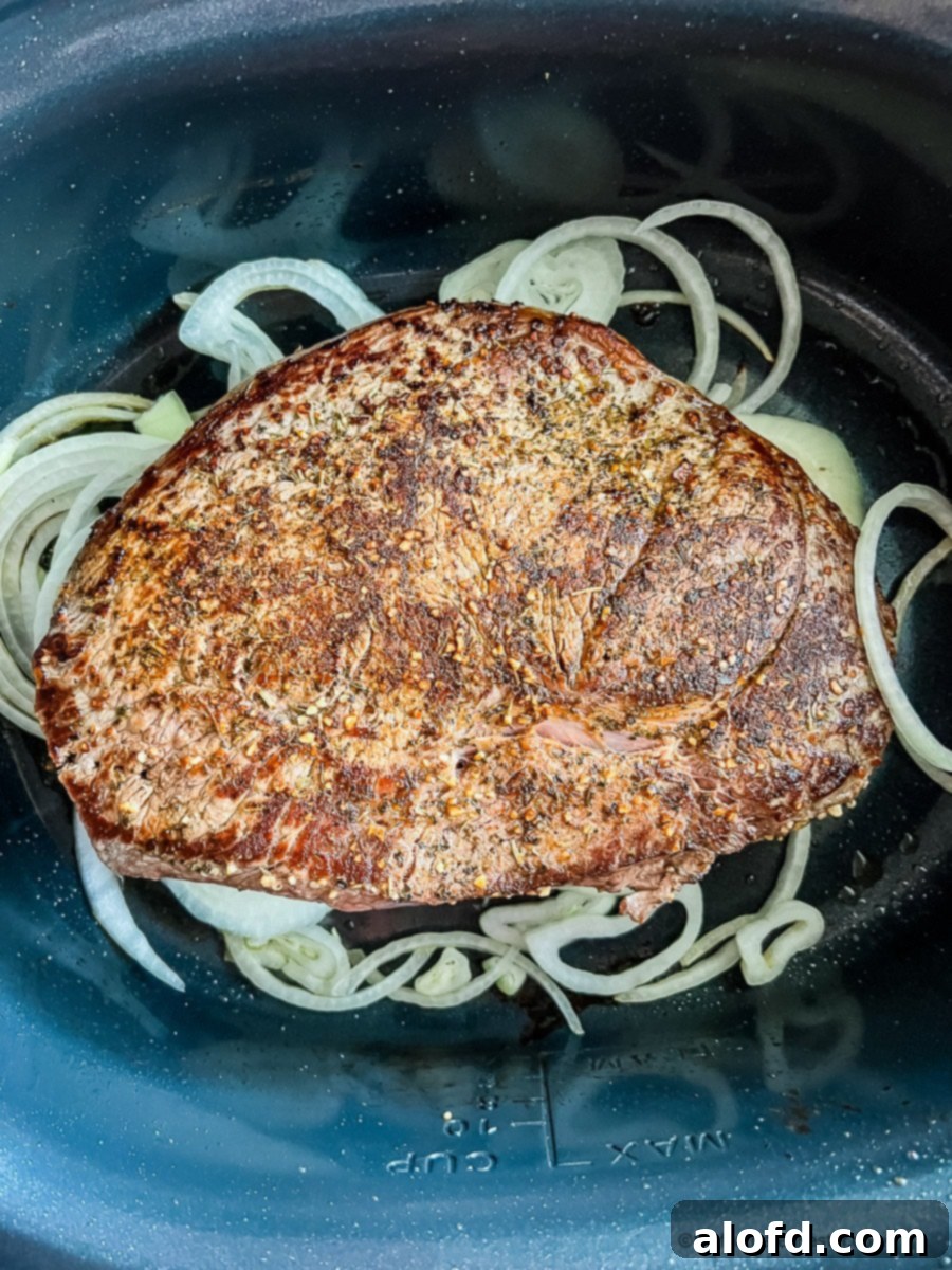 Fall-Apart Slow Cooker Sirloin Tip Roast 8 Seared meat in crockpot with raw onion slices.