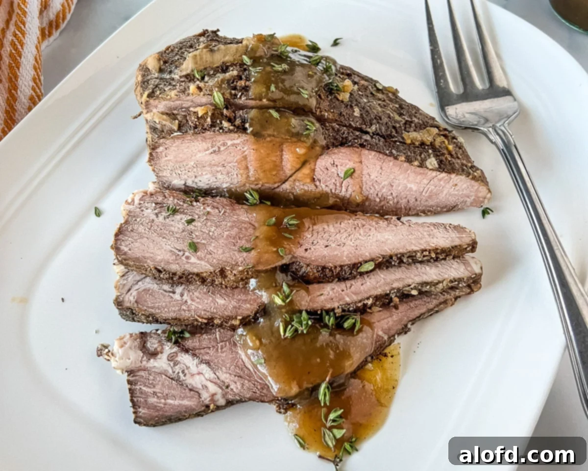 Fall-Apart Slow Cooker Sirloin Tip Roast 10 Juicy, tender beef slices on a white plate.