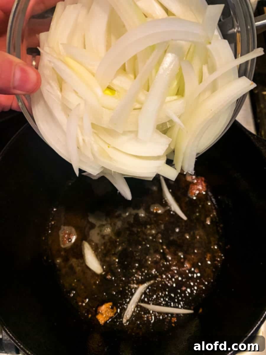 Pouring sliced white onion into pan of bacon grease.