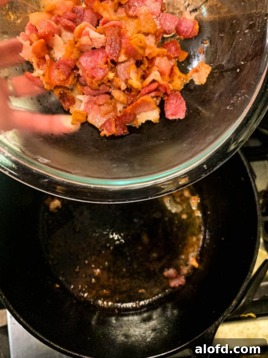 Crispy bacon pieces in glass bowl above pan of bacon grease.