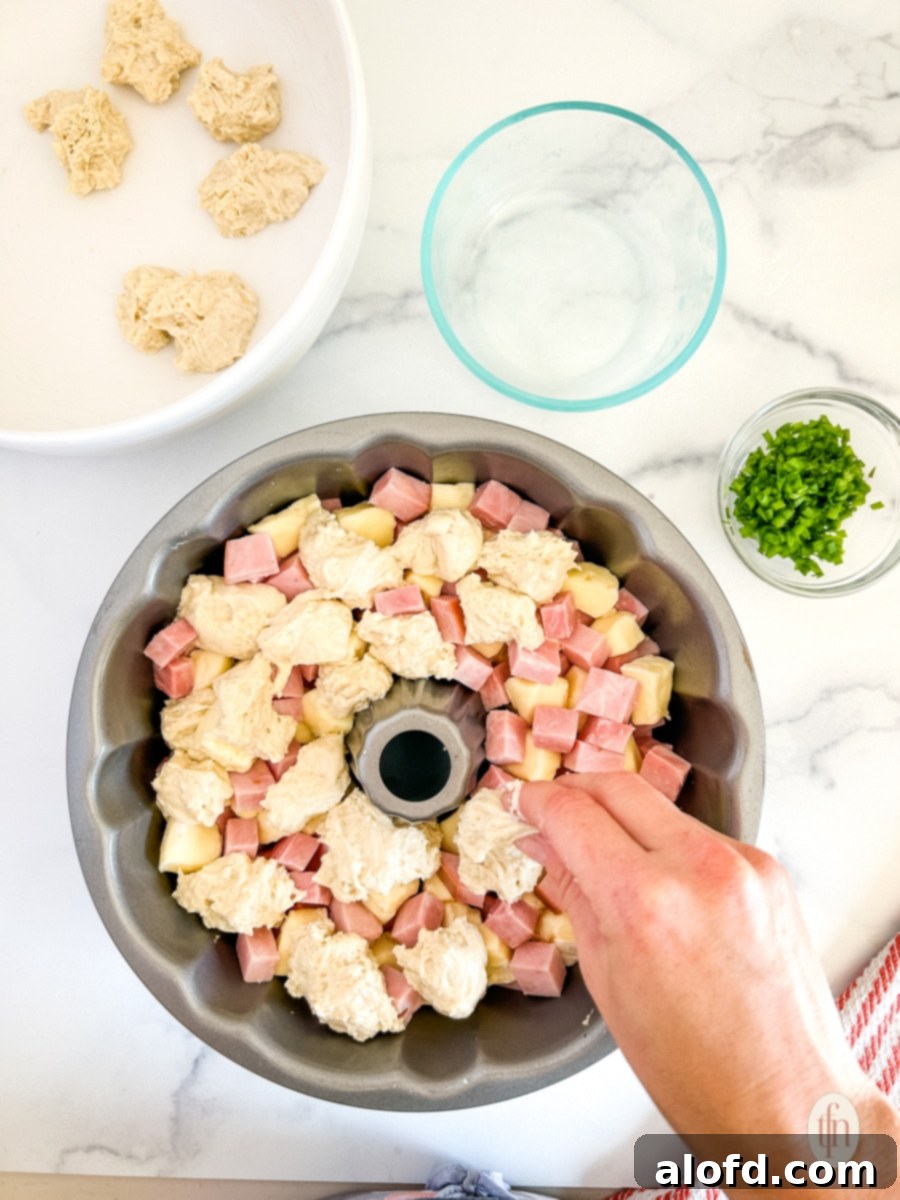 Adding dough into the pan to make monkey bread with ham and brie.