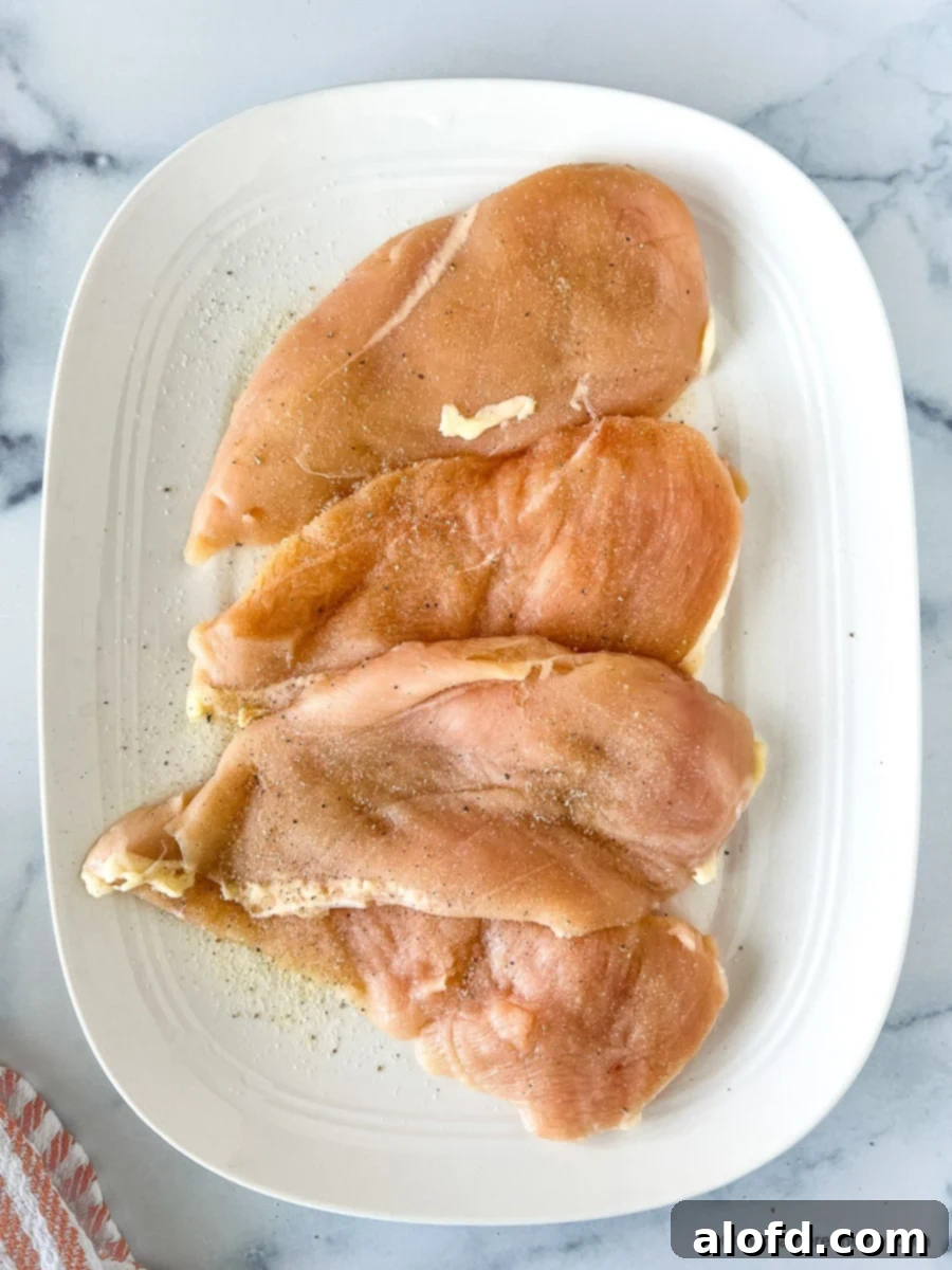 Perfectly Seared Cast Iron Chicken Breast 4 Uncooked seasoned poultry on a white platter.