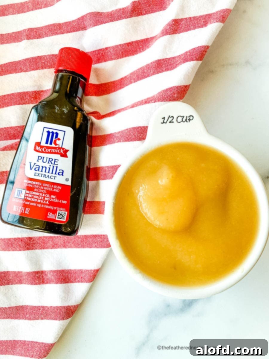 Scrumptious Egg Free Chocolate Chip Cookies 5 A bottle of vanilla extract stands next to a measuring cup filled with unsweetened applesauce, highlighting two crucial liquid ingredients for the eggless cookie recipe.