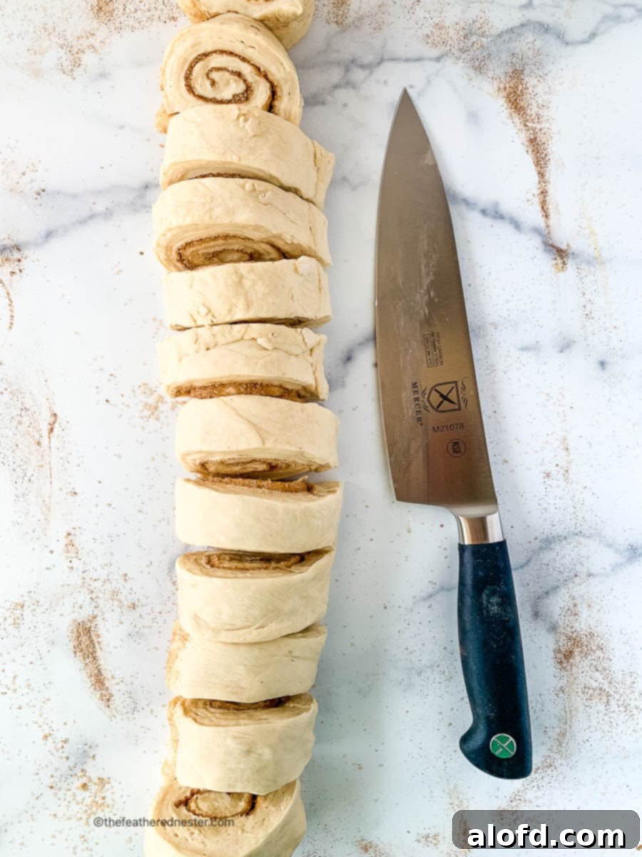 Fluffy Sourdough Discard Cinnamon Rolls 11 A sharp chef's knife positioned next to neatly sliced cinnamon roll dough pieces on a marble countertop.