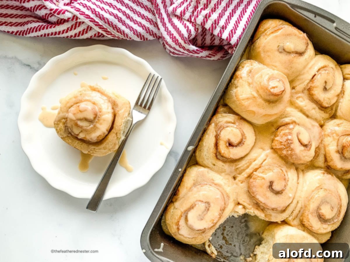 Fluffy Sourdough Discard Cinnamon Rolls 3 A baking pan filled with frosted sourdough cinnamon rolls, with one perfectly plated roll beside it.