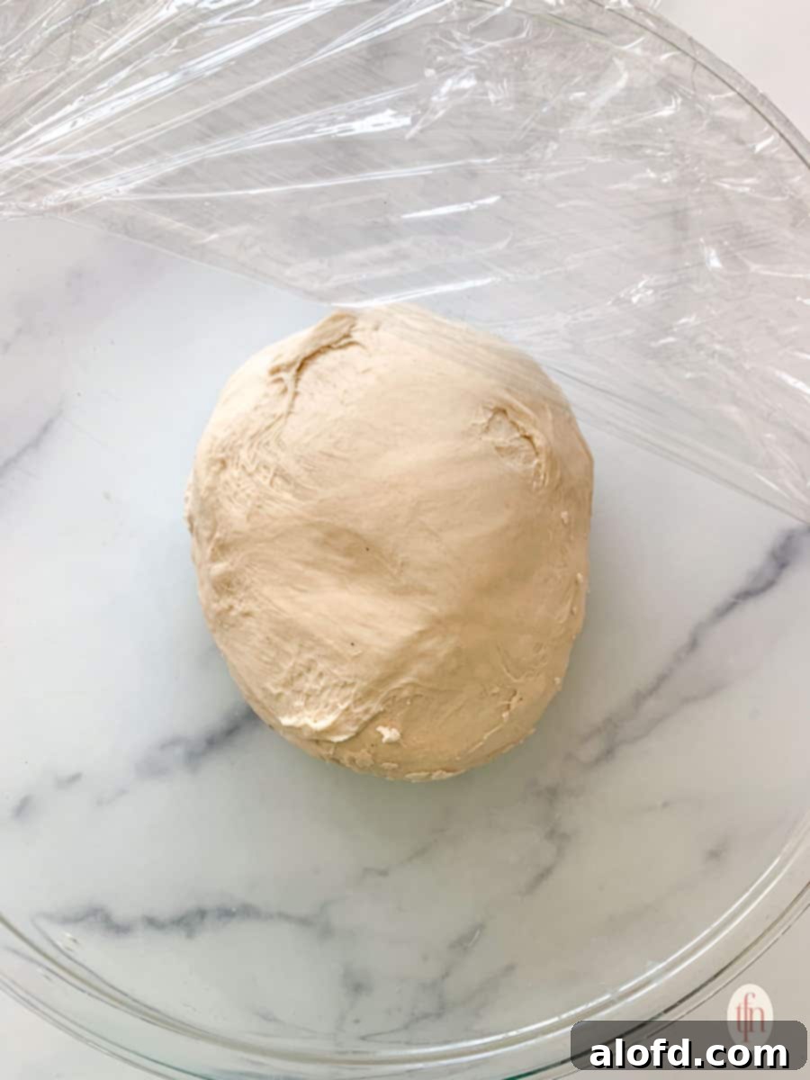 Fluffy Sourdough Discard Cinnamon Rolls 7 A ball of sourdough dough in a glass bowl, covered with plastic wrap, resting for its first rise.